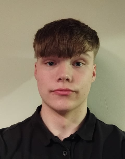 Portrait of a young person with dark brown hair and bangs, wearing a black collared shirt against a neutral background